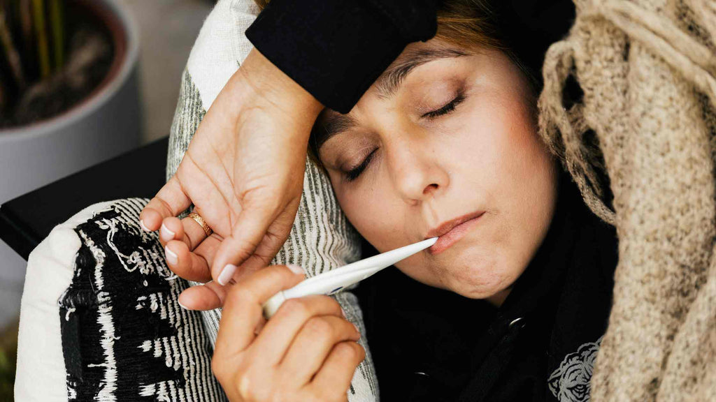 person laying on couch with thermometer feeling sick by apothecary brands